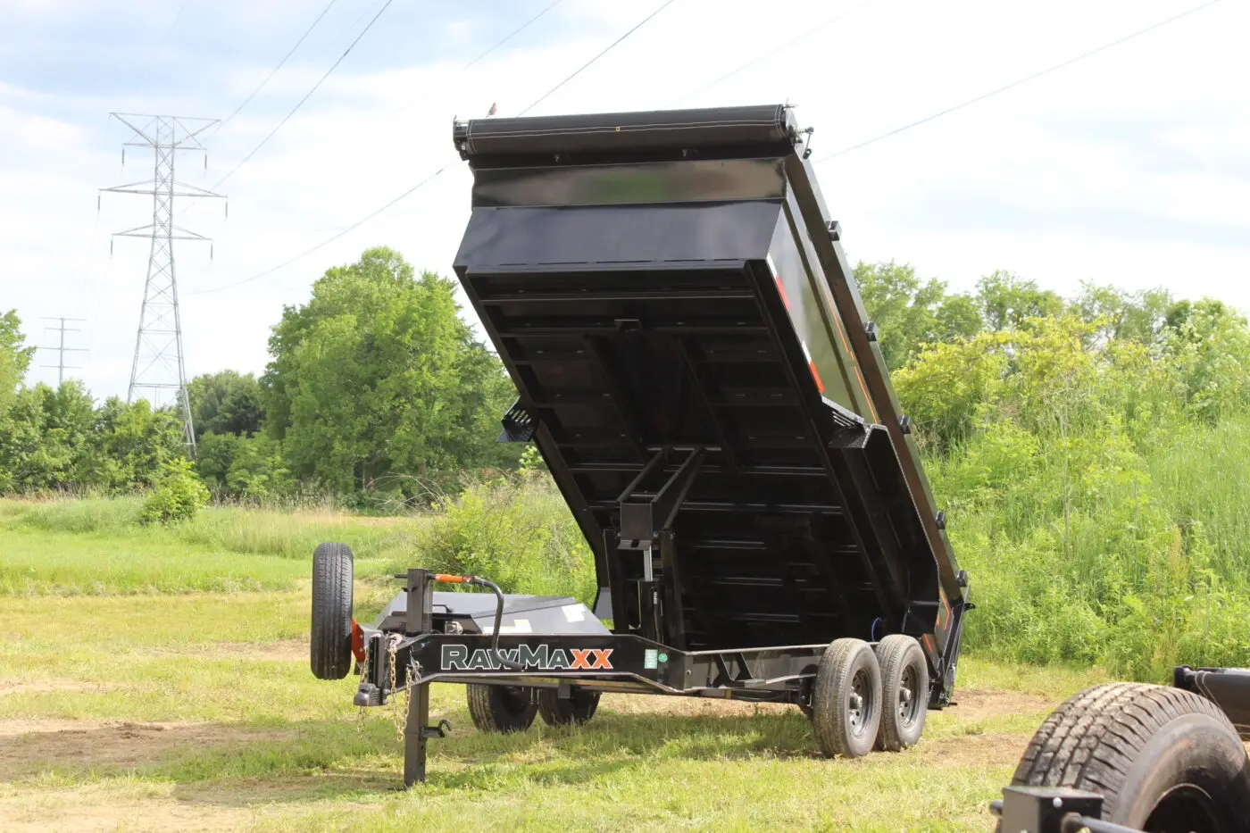Black dump trailer raised in grassy field