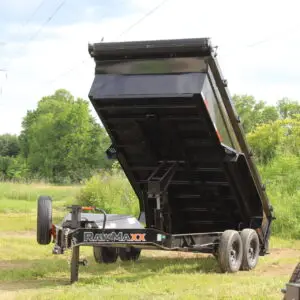 Black dump trailer raised in grassy field