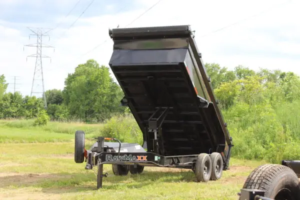 Black dump trailer raised in grassy field